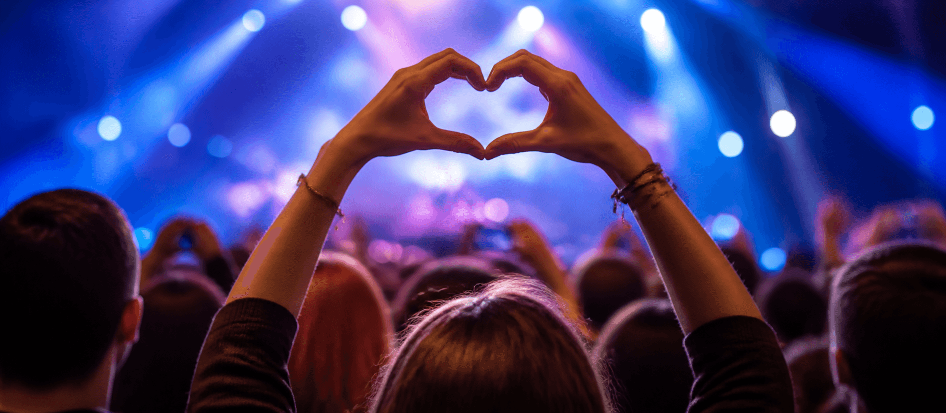 A fan making a heart with their hands at a live event.